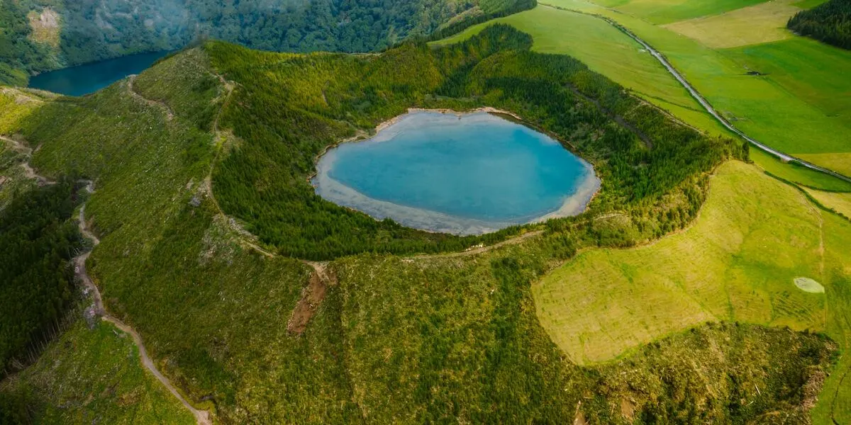 A turquoise crater lake ringed by green pasture and forest on São Miguel in the Azores, seen from the caldera rim